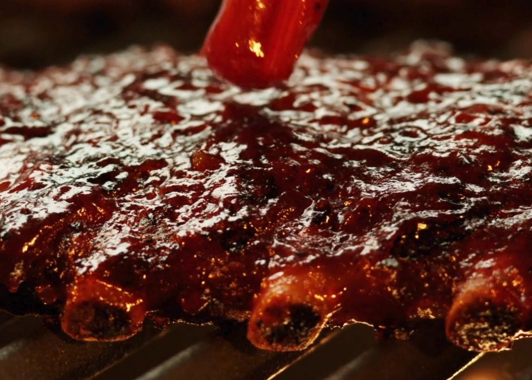 Close-up of house-smoked ribs being brushed with glossy barbecue sauce